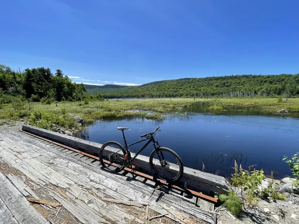 Mountain bike leaning on a wooden dock by a pond and green hills